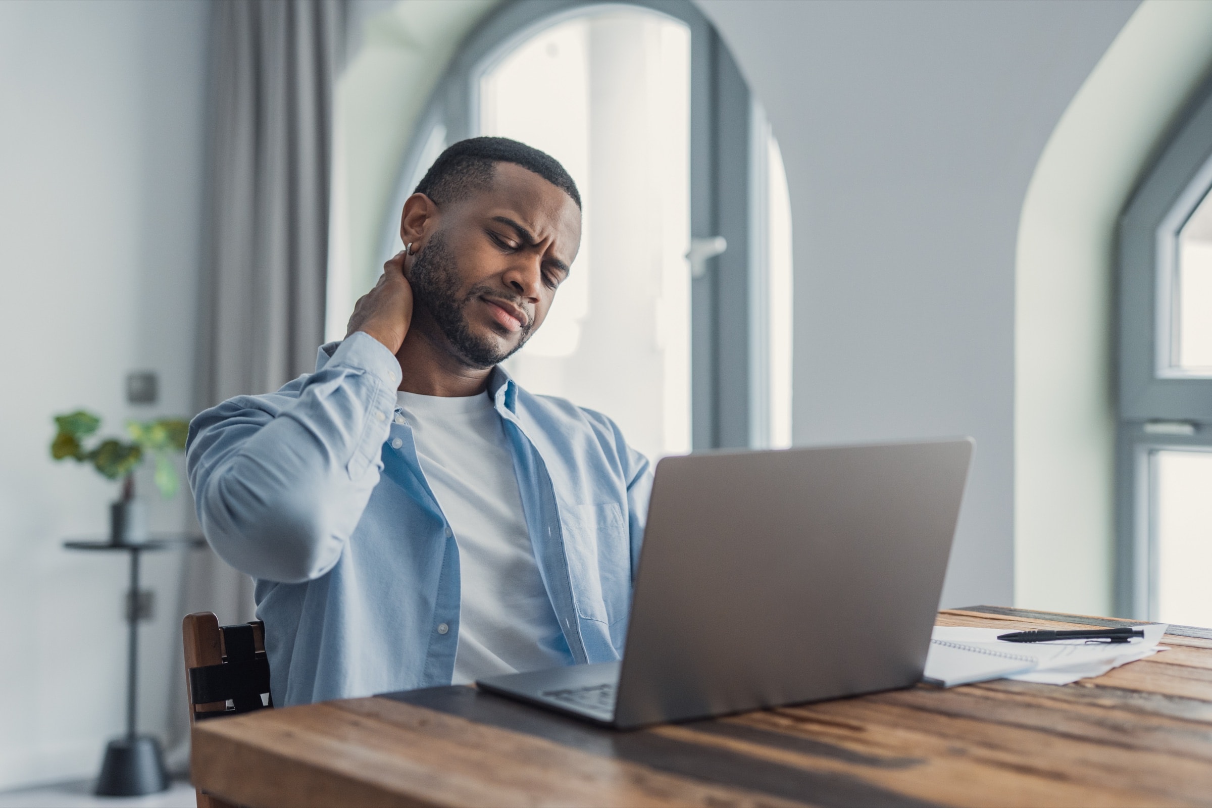 Man at a laptop rubbing his sore neck