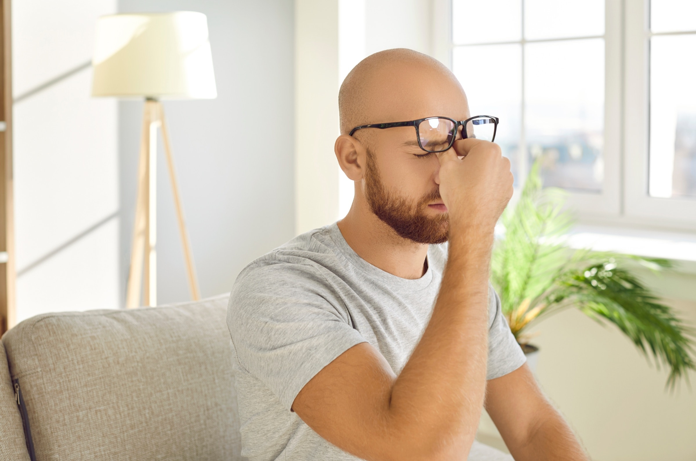 Man in glasses pinching the bridge of his nose from pain behind the eyes