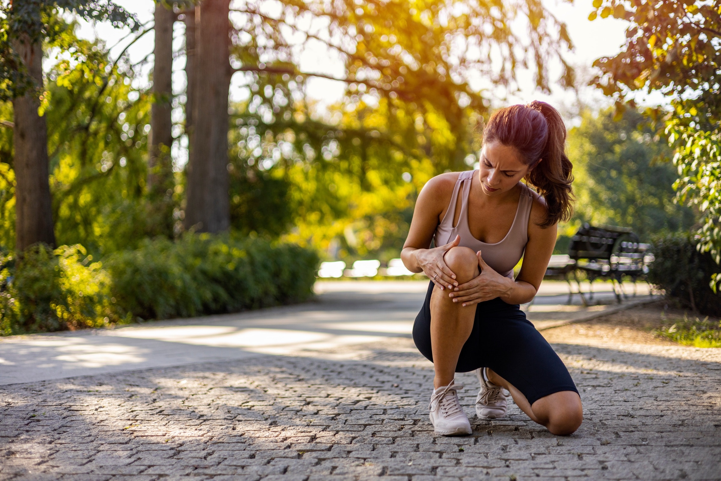 A runner kneeling on a park path holding her knee