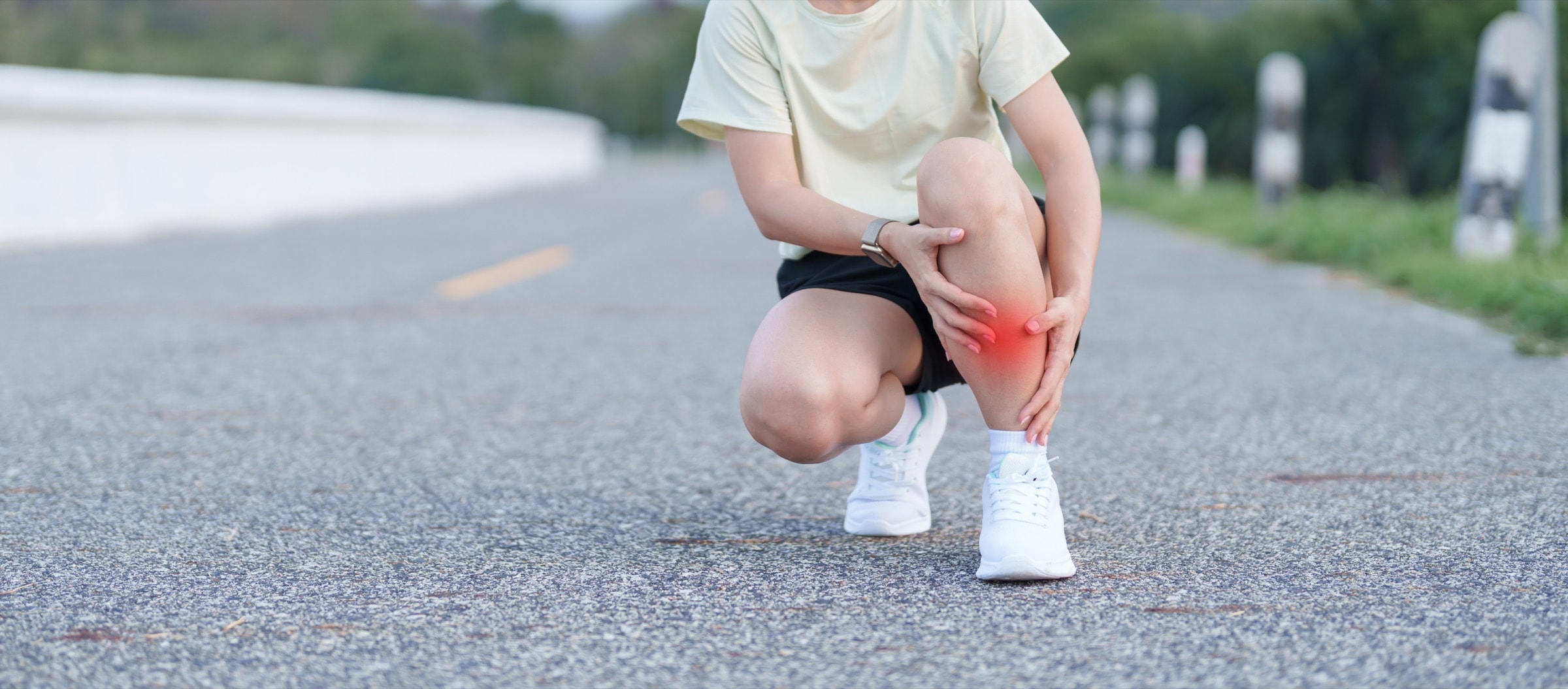 Runner crouching on a road holding her sore lower leg