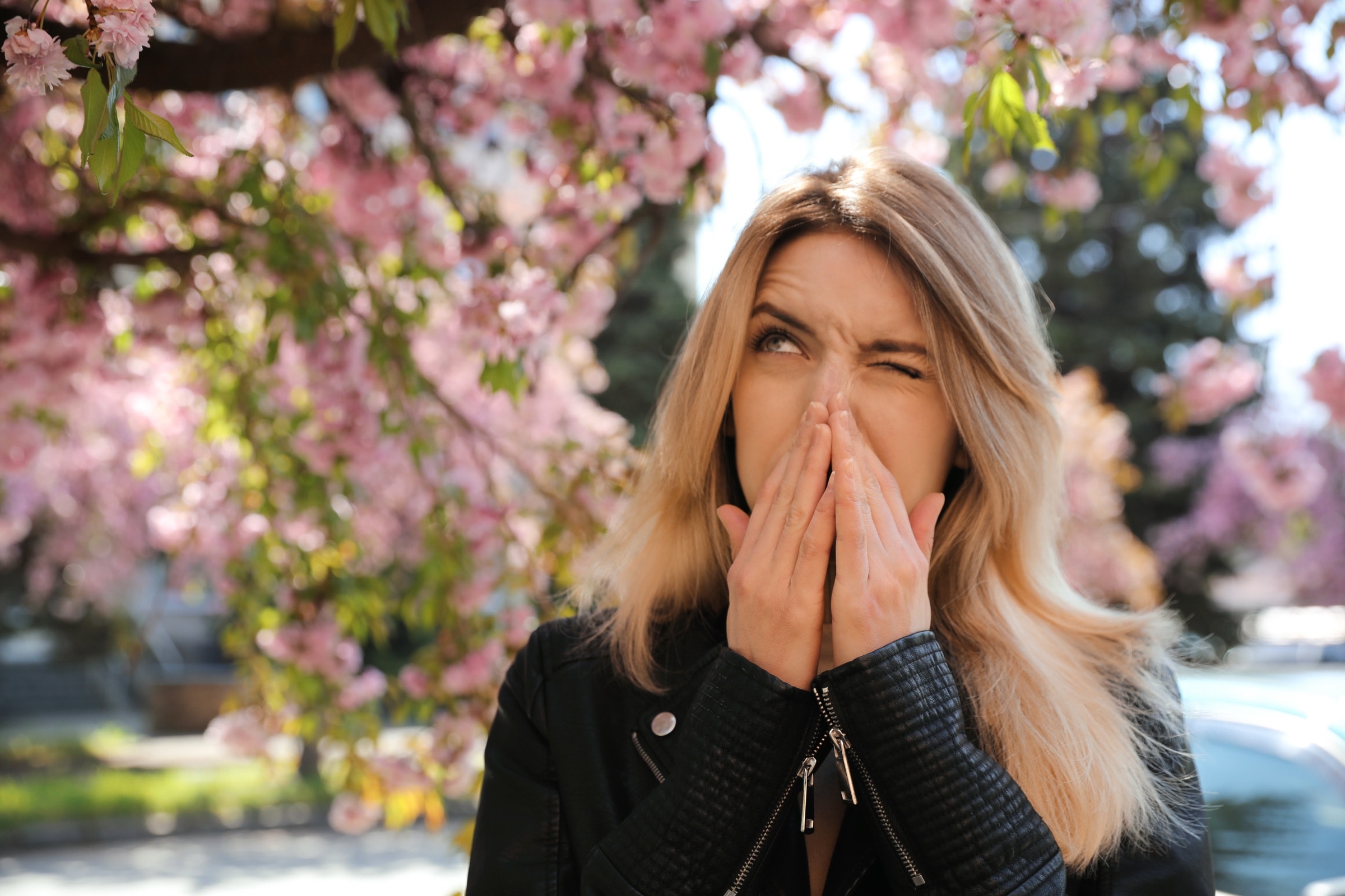 A woman sneezing outdoors under spring blossoms