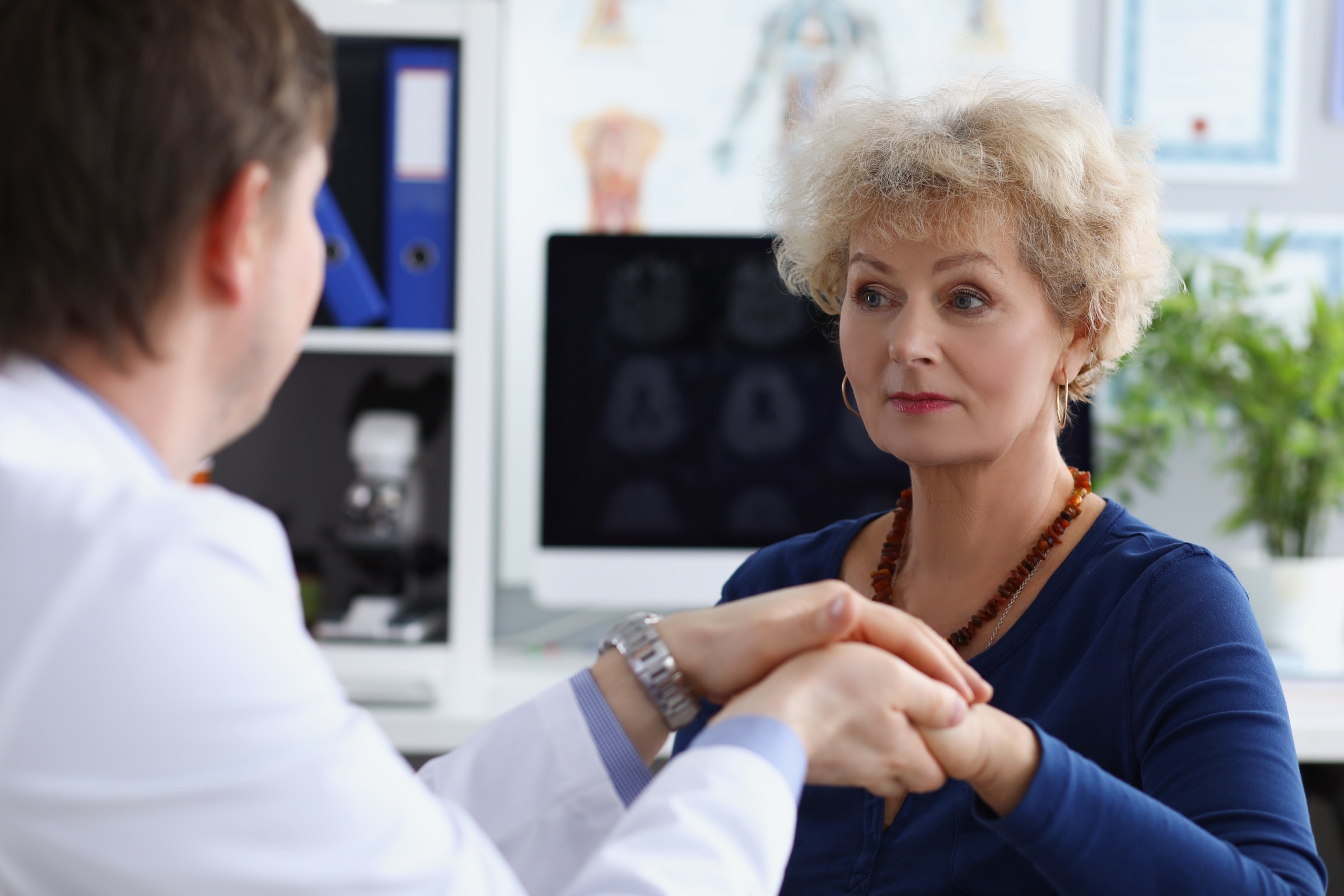 A doctor holding a patient's hands, with brain scans on the screen behind her